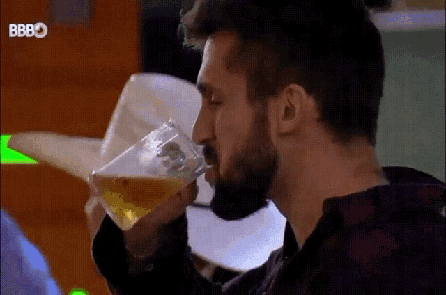 a man with a beard is drinking a glass of beer from a plastic cup .
