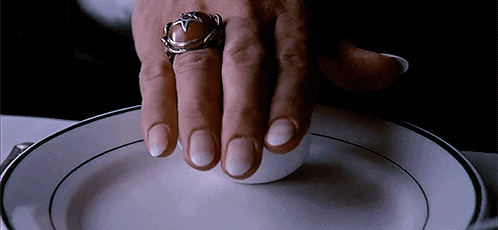 a person wearing a ring holds a cup on a white plate