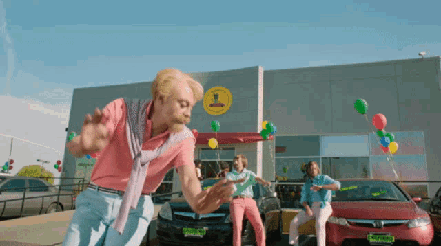 a group of people dancing in front of a car dealership with balloons