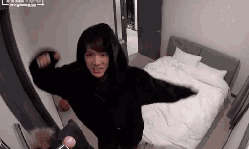 a person in a black hoodie is standing in a bedroom next to a bed .