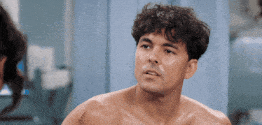a shirtless man with a scar on his chest looks at another man
