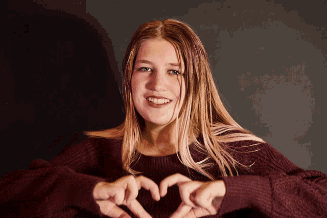 a young woman in a maroon sweater makes a heart shape with her hands