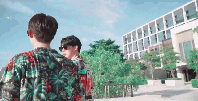 two men wearing sunglasses are standing in front of a building .