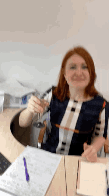 a woman sitting at a desk holding a glass