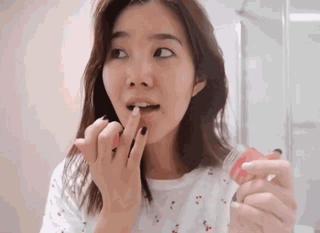 a woman applying lip balm to her lips while holding a jar of lip balm