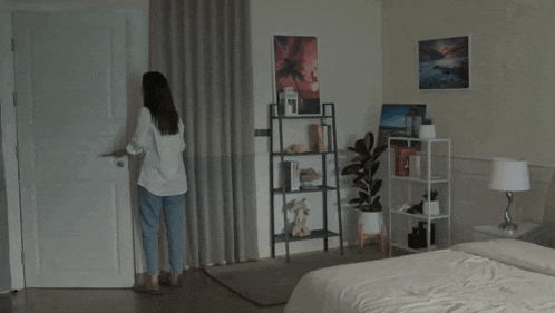 a woman stands in a bedroom with a bed and a shelf