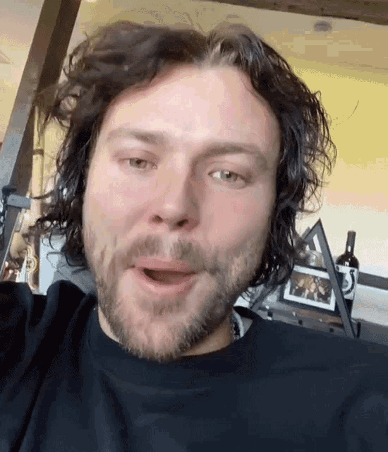 a man with curly hair and a beard is wearing a black shirt and making a funny face .