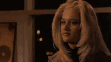 a woman with long blonde hair is standing in front of a window at night with her eyes closed .