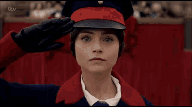 a woman wearing a red hat and gloves salutes in front of a red curtain .