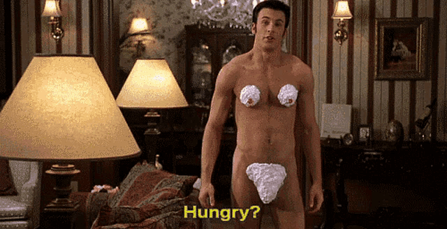 a naked man with whipped cream on his chest is standing in a living room and asking if he is hungry
