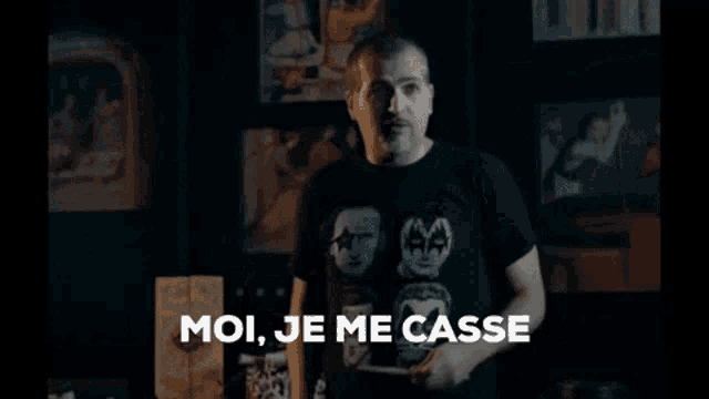 a man in a black t-shirt is standing in front of a wall with a kiss shirt on .