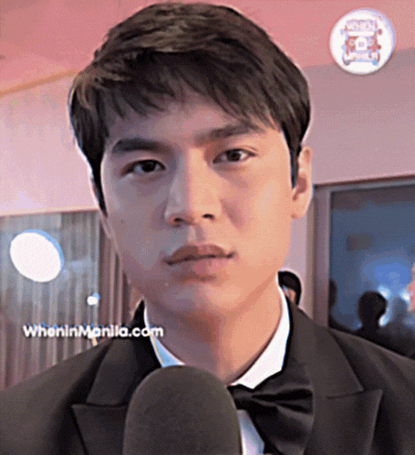 a man in a tuxedo talks into a microphone with wheninmanila.com written on the bottom right