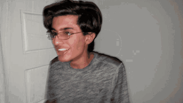 a young man wearing glasses and a gray shirt is smiling