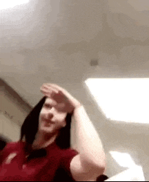 a woman in a red shirt is covering her face with her hand in a room .