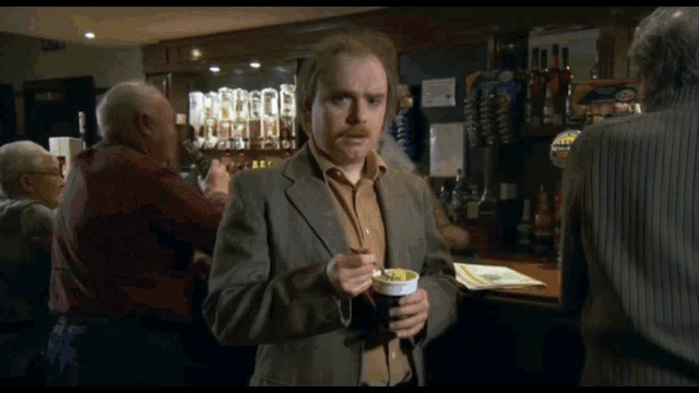 a man in a suit is holding a cup of coffee and says i 'll dae it