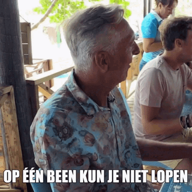 a man in a floral shirt says op een been kun je niet lopen in a foreign language