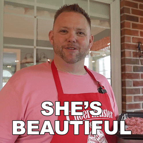 a man wearing a pink shirt and red apron says she 's beautiful in white letters