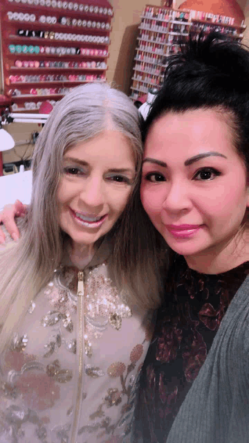 two women posing for a picture in front of a wall of nail polishes