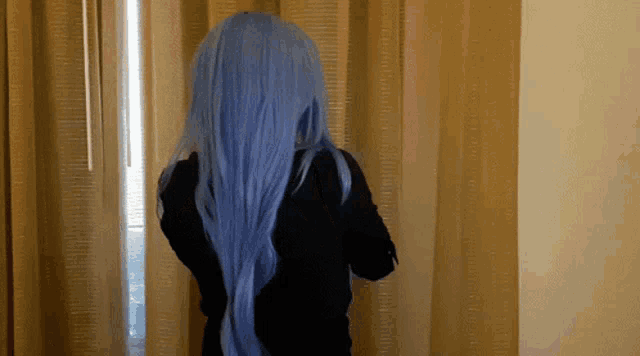 a person with long blue hair stands in front of a window