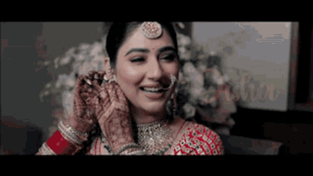 a woman in a red and gold dress is smiling and putting on her earrings