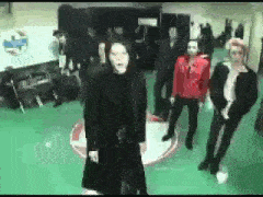 a group of people are standing on a green floor and one of them is wearing a black coat .