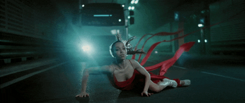 a woman in a red dress is crawling on the ground in front of a truck