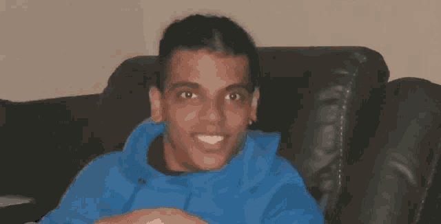 a man in a blue hoodie is smiling while sitting in a chair