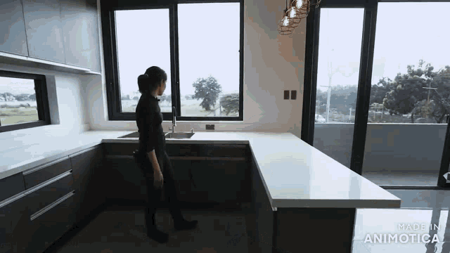 a woman is standing in a kitchen with a sink and a lot of windows .