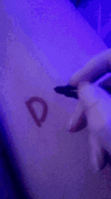 a person is writing a heart on their wrist with a pen .