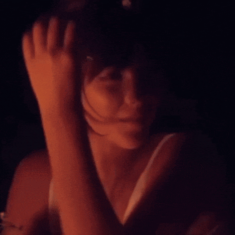 a woman wearing sunglasses looks at the camera in a dark room
