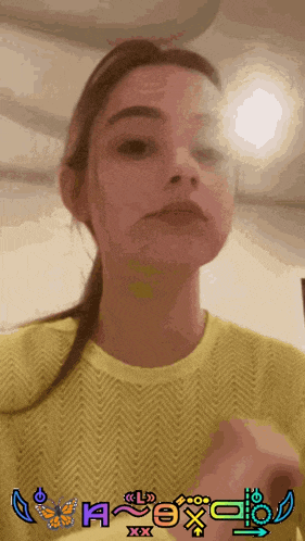 a woman wearing a yellow sweater has a picture of a butterfly and the letter h on her face