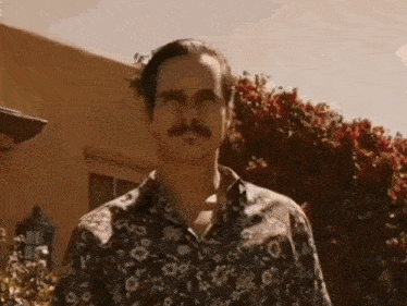 a man with a mustache is standing in front of a house .