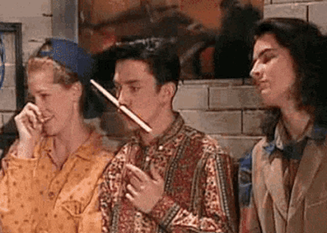 a group of people are standing next to each other and one of them is holding a pencil in his nose .