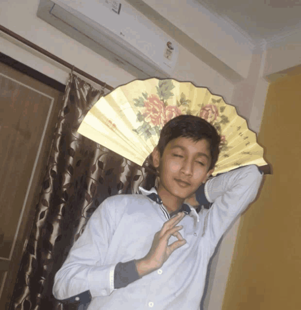 a young boy holds a fan over his head in front of an air conditioner
