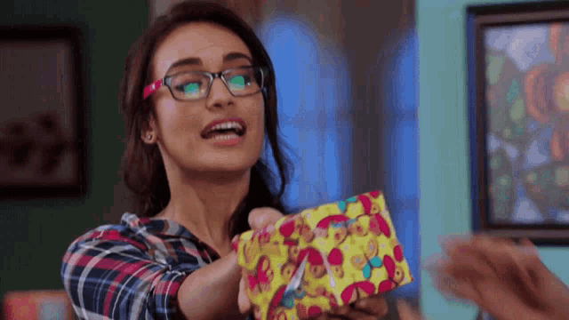 a woman wearing glasses is holding a colorful gift