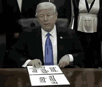 a man in a suit and tie is sitting at a desk signing a document