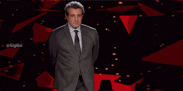 a man in a suit and tie is standing in front of a black background with red triangles ..