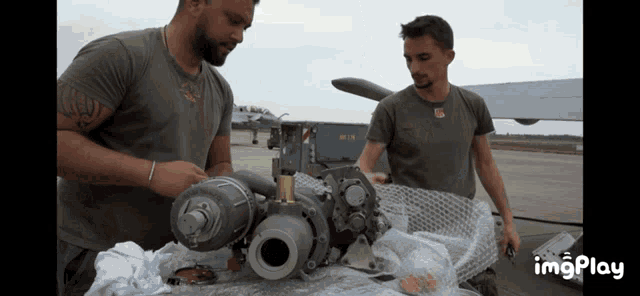 two men are working on a piece of equipment with a gif that says imgplay at the bottom