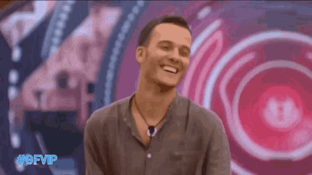 a man in a grey shirt is smiling in front of a pink background with #ofvip in blue letters