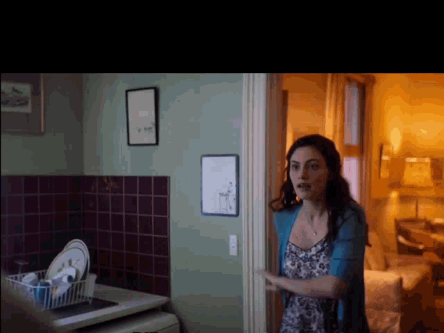 a woman standing in a kitchen with a picture on the wall that says ' i 'm sorry '