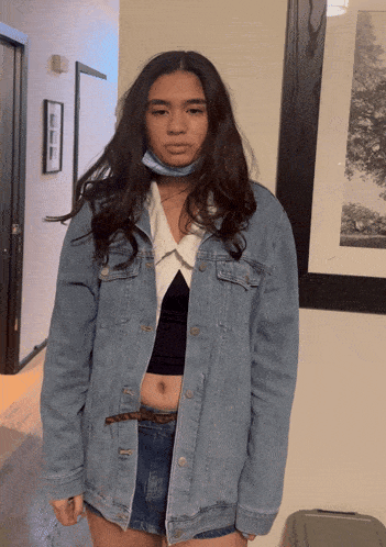 a woman wearing a denim jacket and shorts stands in front of a picture