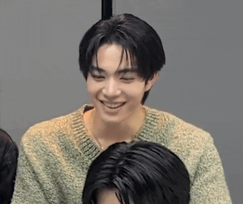 a young man wearing a green sweater is smiling while sitting next to another man .
