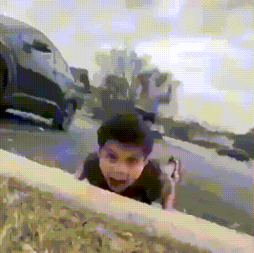 a young boy is crawling over a fence while a car is parked in the background