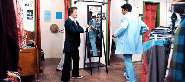 a man in a blue suit is standing next to another man in a black suit in front of a mirror