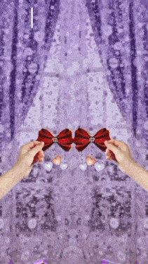 two hands holding a red bow with hearts hanging from it in front of a purple curtain