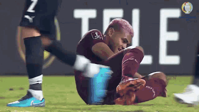 a soccer player with pink hair is laying on the ground with the word tele in the background