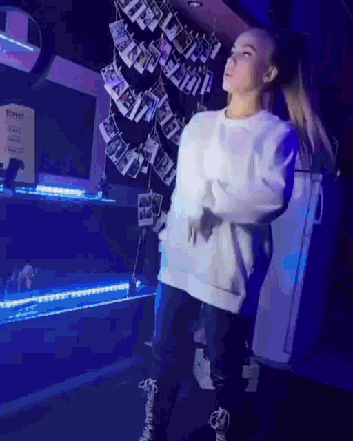 a girl in a white sweatshirt is dancing in front of a sign that says " tommy "