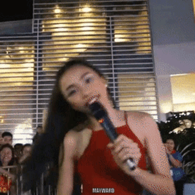 a woman in a red top is singing into a microphone that says hayward on the bottom