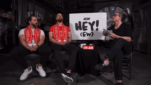 three men sit in front of a sign that says " hey "