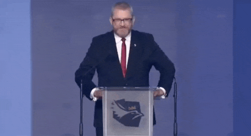 a man in a suit and red tie is standing at a podium